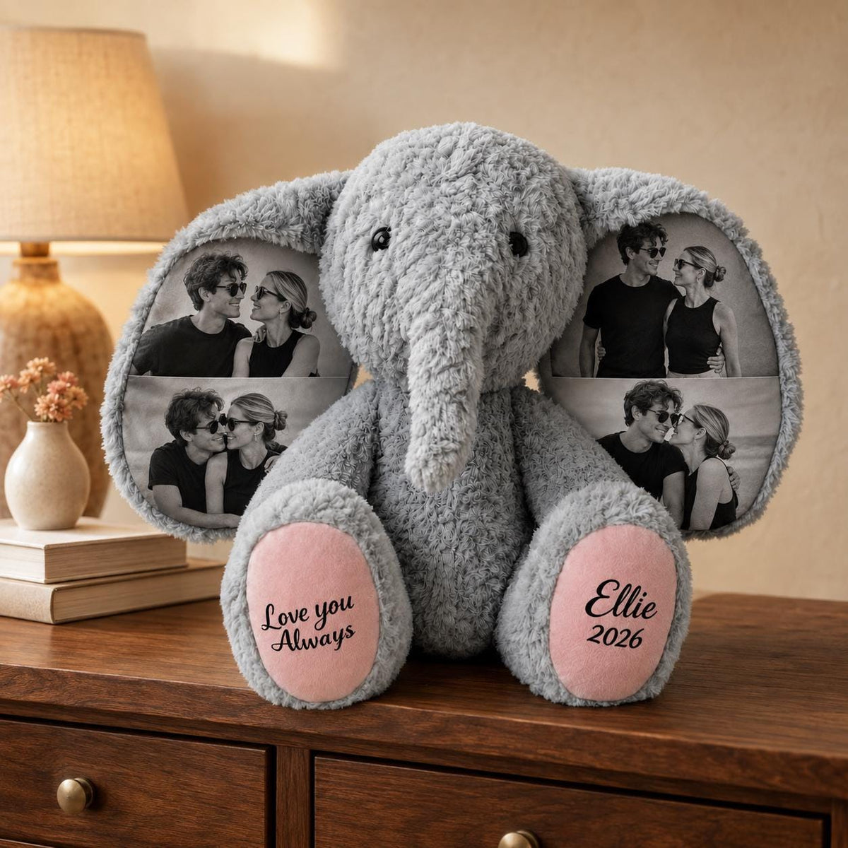A gray plush elephant toy featuring large ears printed with black and white photographs of a couple. The elephant has pink foot pads with the text Love you Always on the left foot and the name Ellie and the year 2026 on the right.
