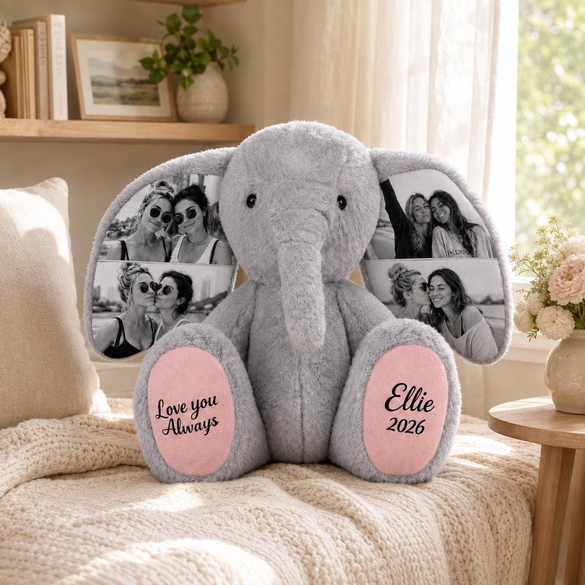A gray plush elephant toy featuring large ears printed with black and white photographs of people. The pink foot pads are embroidered with the text Love you Always on the left and the name Ellie and the year 2026 on the right.