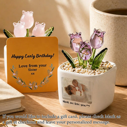 Two decorative glass tulip flower arrangements in white square pots. One pot has a card that reads "Happy Early Birthday! Love from your Sister." The other pot has a photo and the text "Mom, we love you."