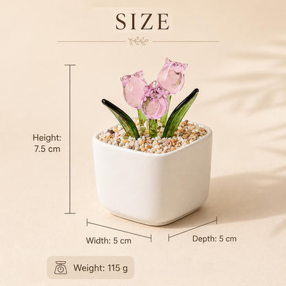 A small, white square ceramic pot with three pink glass tulip flowers and green leaves. The pot is filled with small pebbles. The height is 7.5 cm, width and depth are 5 cm, and the weight is 115 g.