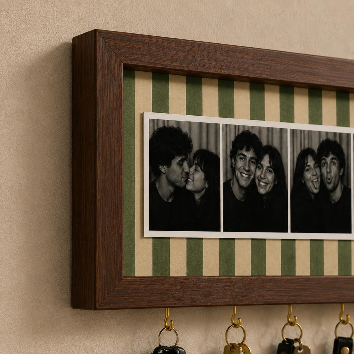 A rectangular dark wood wall-mounted key holder featuring a central horizontal strip of green and beige vertical stripes. The frame displays a series of three black and white photographs of a couple, with four brass hooks attached below.