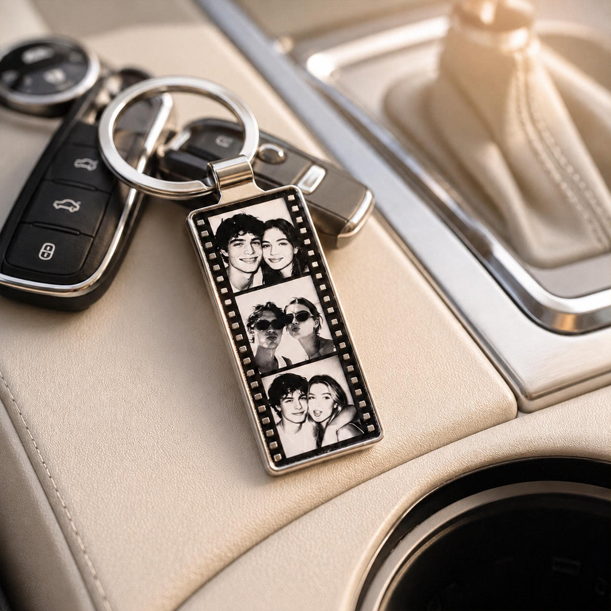 A rectangular metal keychain featuring a vertical film strip design with three black and white photographs of two people. The keychain is attached to a silver metal ring and is positioned next to a black car key fob.