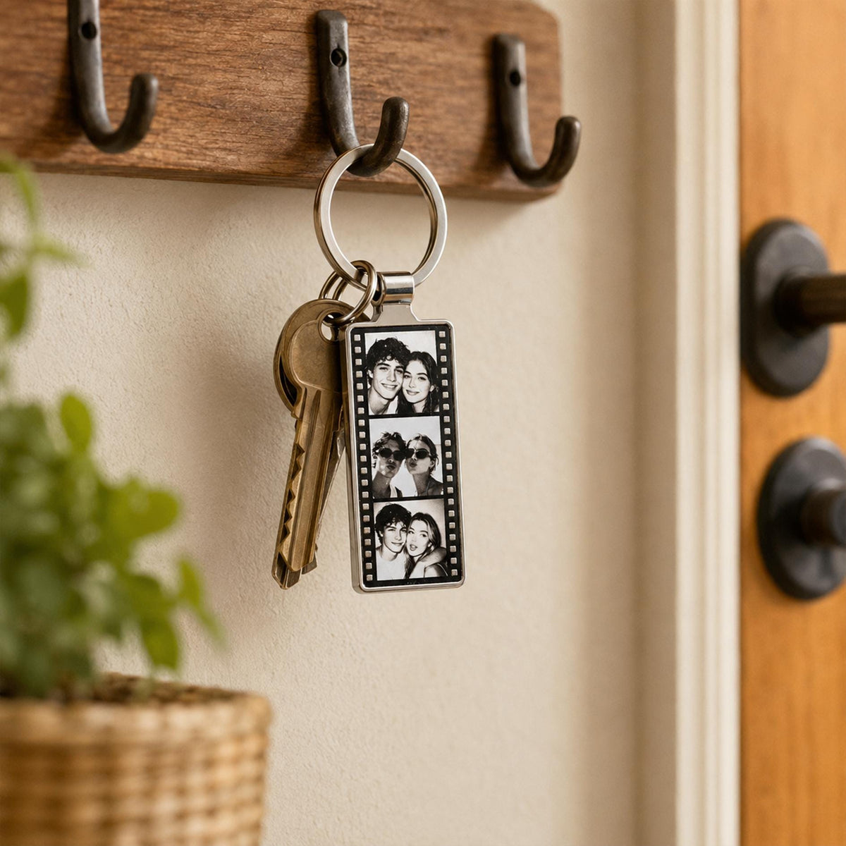 A rectangular metal keychain featuring a vertical film strip design with three black and white portrait photos of two people. The keychain is attached to a silver split ring holding a single brass-colored metal key.