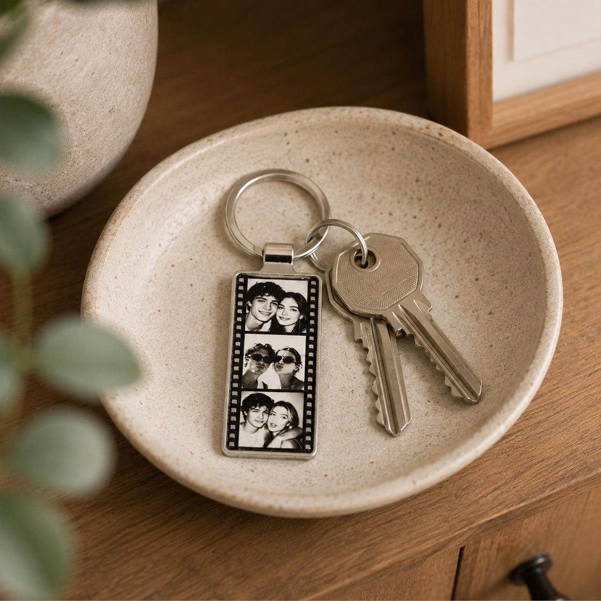 A rectangular silver-toned metal keychain featuring a vertical film strip design with three black and white portrait photos of a couple. The keychain is attached to a circular metal ring holding two silver-colored metal keys.