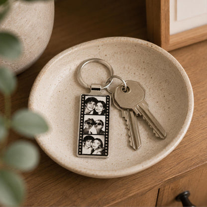 A rectangular silver-toned metal keychain featuring a vertical film strip design with three black and white portrait photos of a couple. The keychain is attached to a circular metal ring holding two silver-colored metal keys.