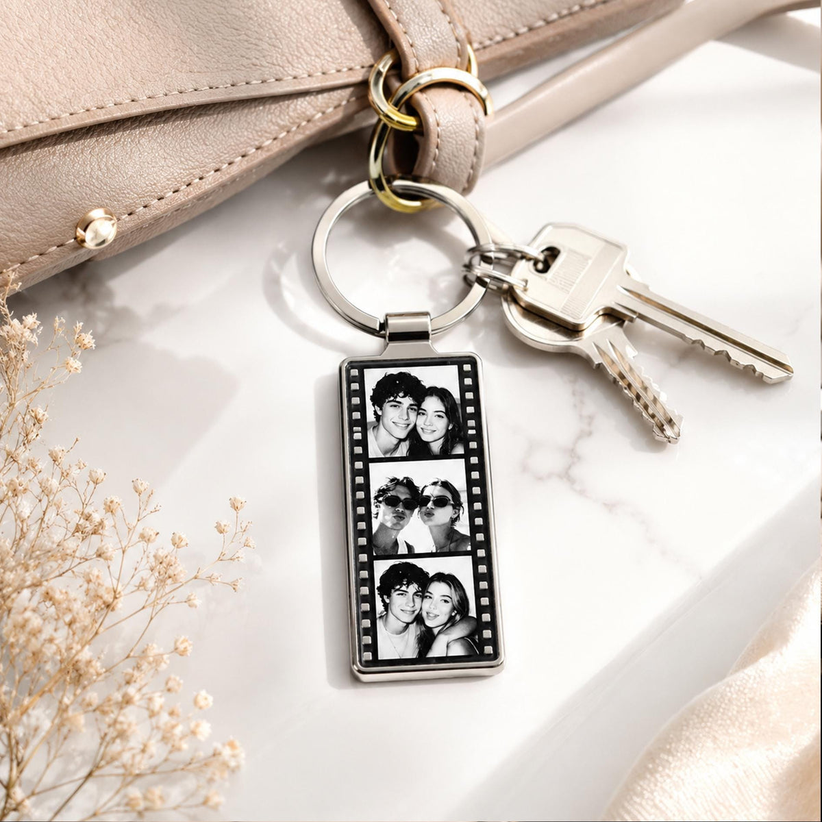 A rectangular silver-toned metal keychain featuring a vertical film strip design. The center contains three stacked black and white photographs of a couple. The keychain is attached to a circular split ring with two silver metal keys.