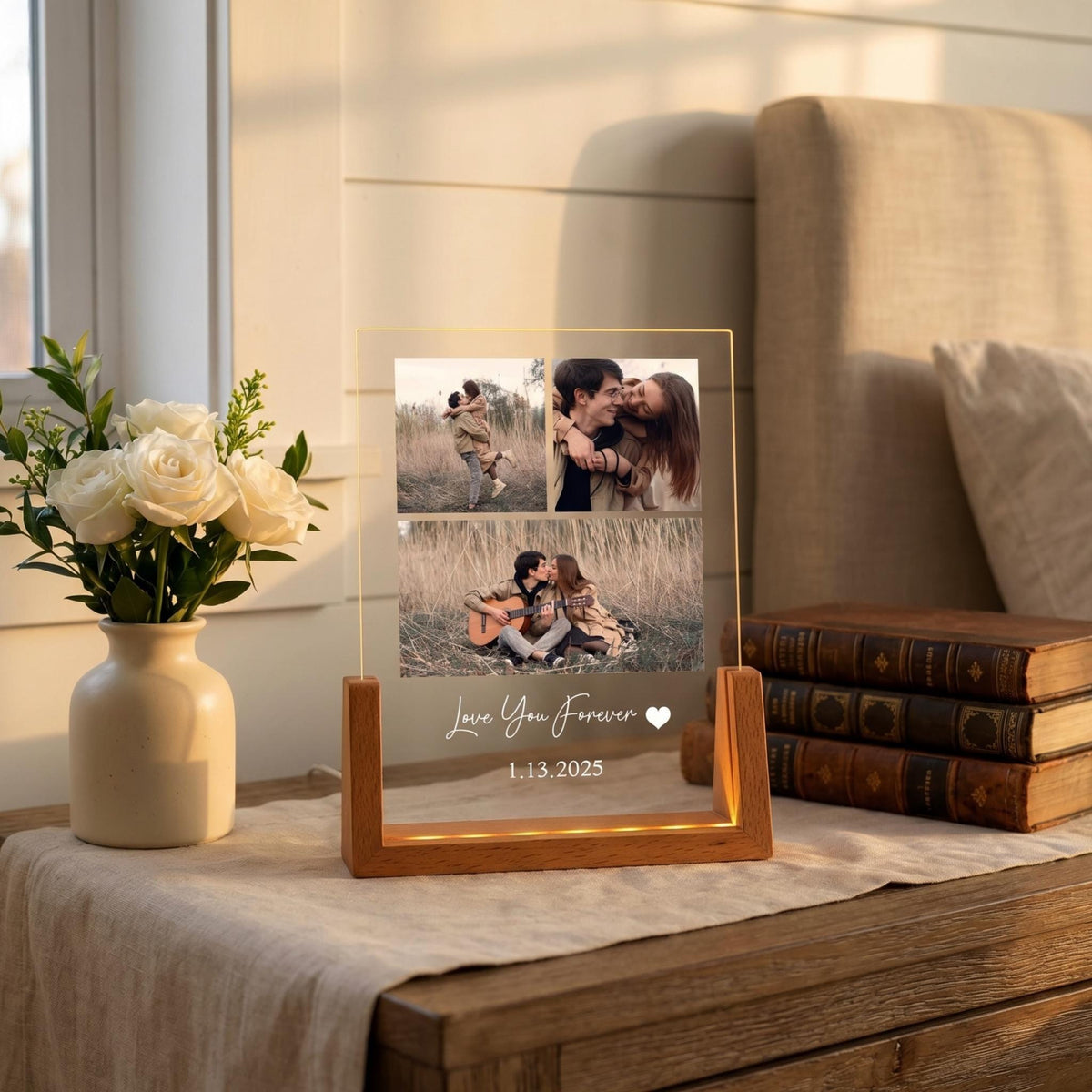 A clear acrylic photo display with a wooden base. The display features three photos of a couple and the text "Love You Forever" and the date "1.13.2025". The base has a warm light.