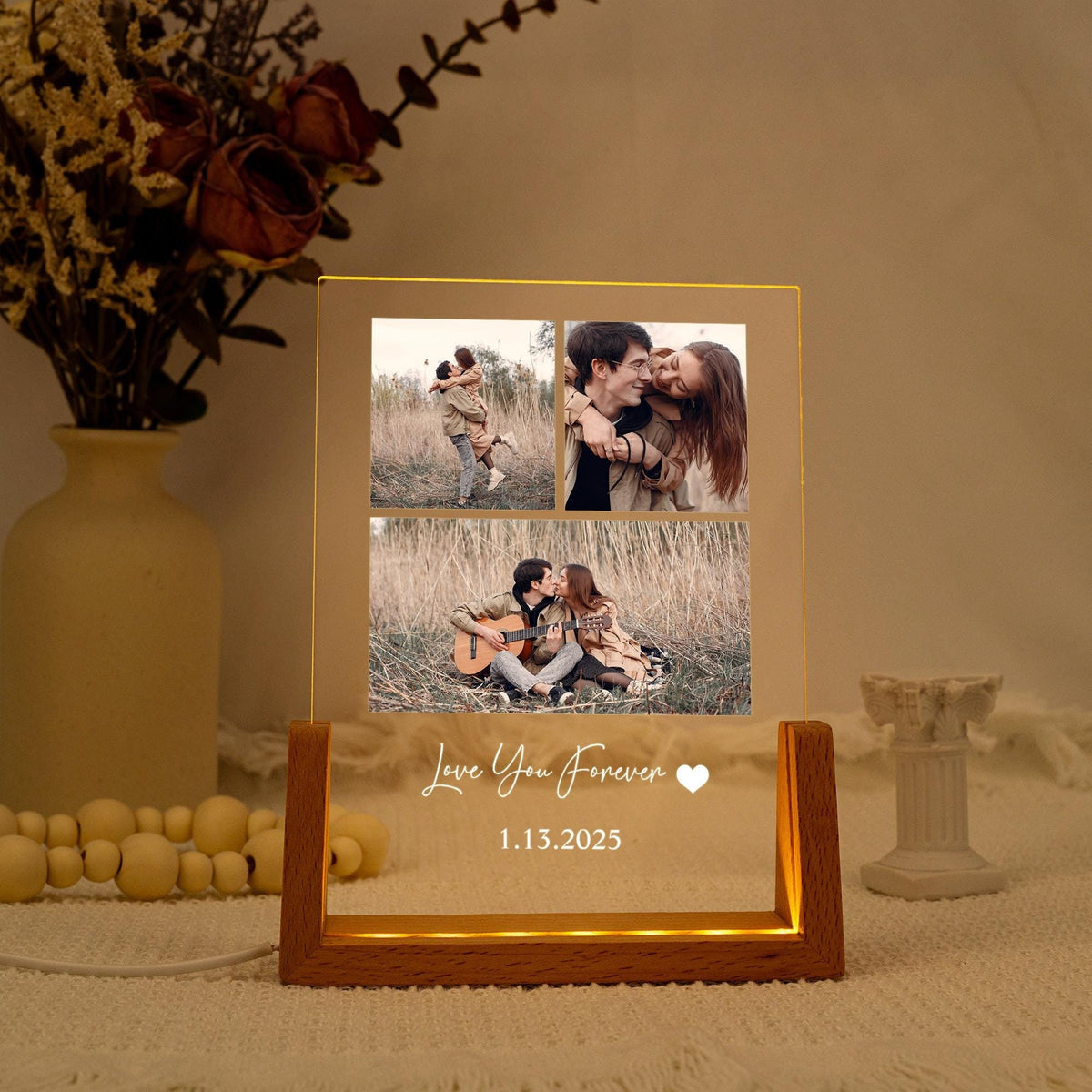 A lighted acrylic photo display with a wooden base. The display features three photos of a couple and the text "Love You Forever" with a heart symbol and the date 1.13.2025. The display is lit with a warm glow.