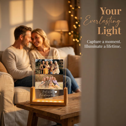 A wooden-based photo frame with two family photos and the text "Best Wish! Full of love for the family 1.6.2025". The frame is illuminated from within, creating a warm glow. The text "Your Everlasting Light" is also visible.