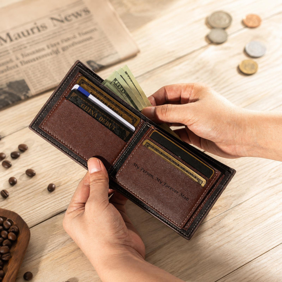 A brown leather bifold wallet with dark brown stitching, featuring multiple card slots and a cash compartment. The interior displays the engraved text "My Person, My Forever Man" on a card slot, with paper currency and cards inserted.