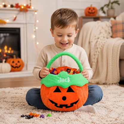 A plush orange pumpkin-shaped Halloween candy bucket with a bright green handle and trim. The bucket features a black felt jack-o'-lantern face and the name Jack embroidered in white thread on the front, filled with assorted candies.