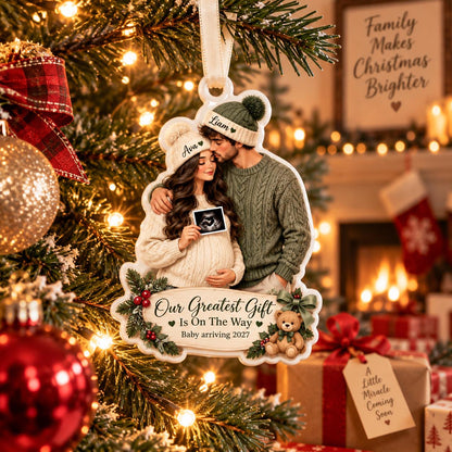 May include: A white, custom-shaped Christmas ornament featuring an illustration of a couple wearing beanies labeled Ava and Liam. The woman holds an ultrasound image. Text reads: Our Greatest Gift Is On The Way, Baby arriving 2027.