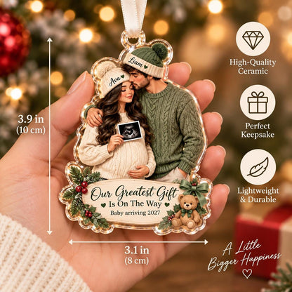 May include: A ceramic Christmas ornament measuring 3.9 inches by 3.1 inches featuring a couple in winter hats with the names Ava and Liam. The ornament displays an ultrasound image, a teddy bear, and the text Our Greatest Gift Is On The Way.
