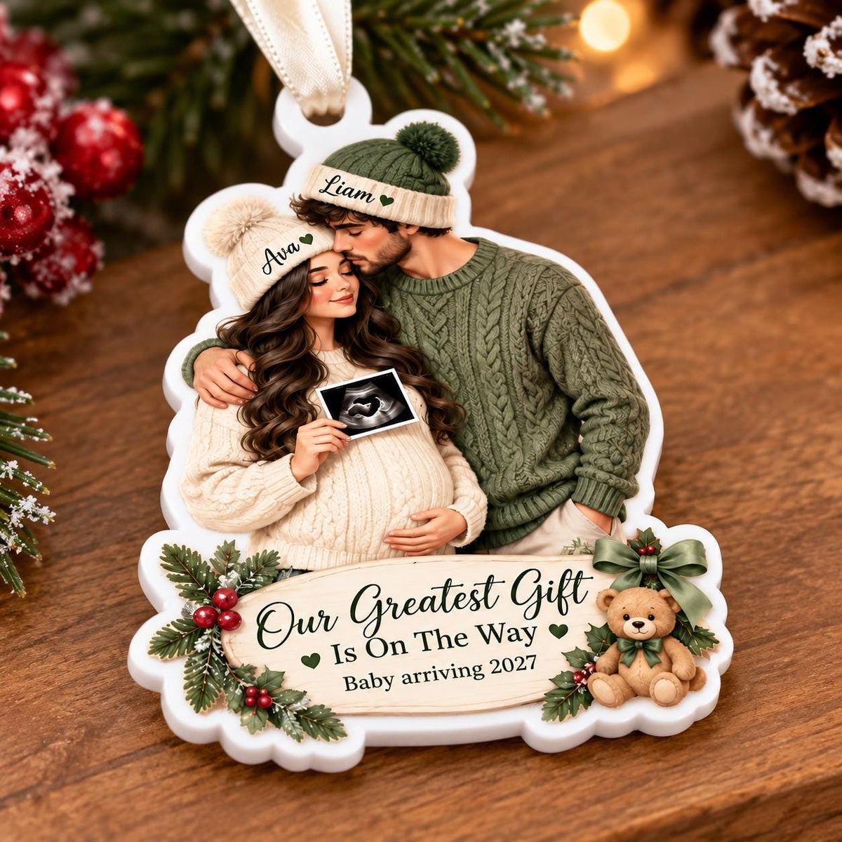 May include: A white Christmas ornament featuring an illustration of a pregnant person and a partner wearing matching green knit hats labeled Ava and Liam. They hold an ultrasound image. The text reads Our Greatest Gift Is On The Way Baby arriving 2027.