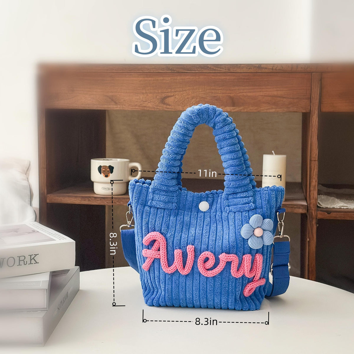 Blue corduroy tote bag with the name "Avery" in pink script. The bag has a flower accent and a shoulder strap. It measures 11 inches wide and 8.3 inches high.