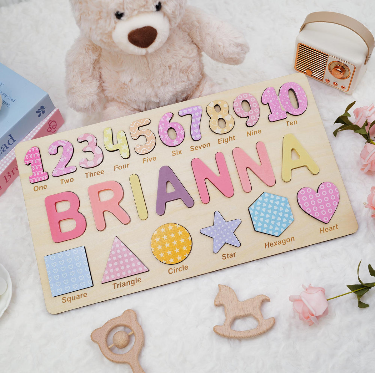 A rectangular wooden puzzle board featuring the name BRIANNA in large, colorful letters, numbers one through ten, and various shapes including a square, triangle, circle, star, hexagon, and heart, each labeled with its name.