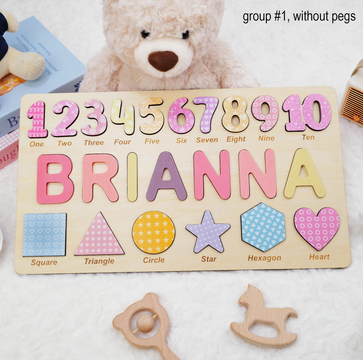 A wooden puzzle board featuring the name BRIANNA in large colorful letters, numbers one through ten with corresponding words, and six shapes labeled square, triangle, circle, star, hexagon, and heart. The text group #1, without pegs is visible.