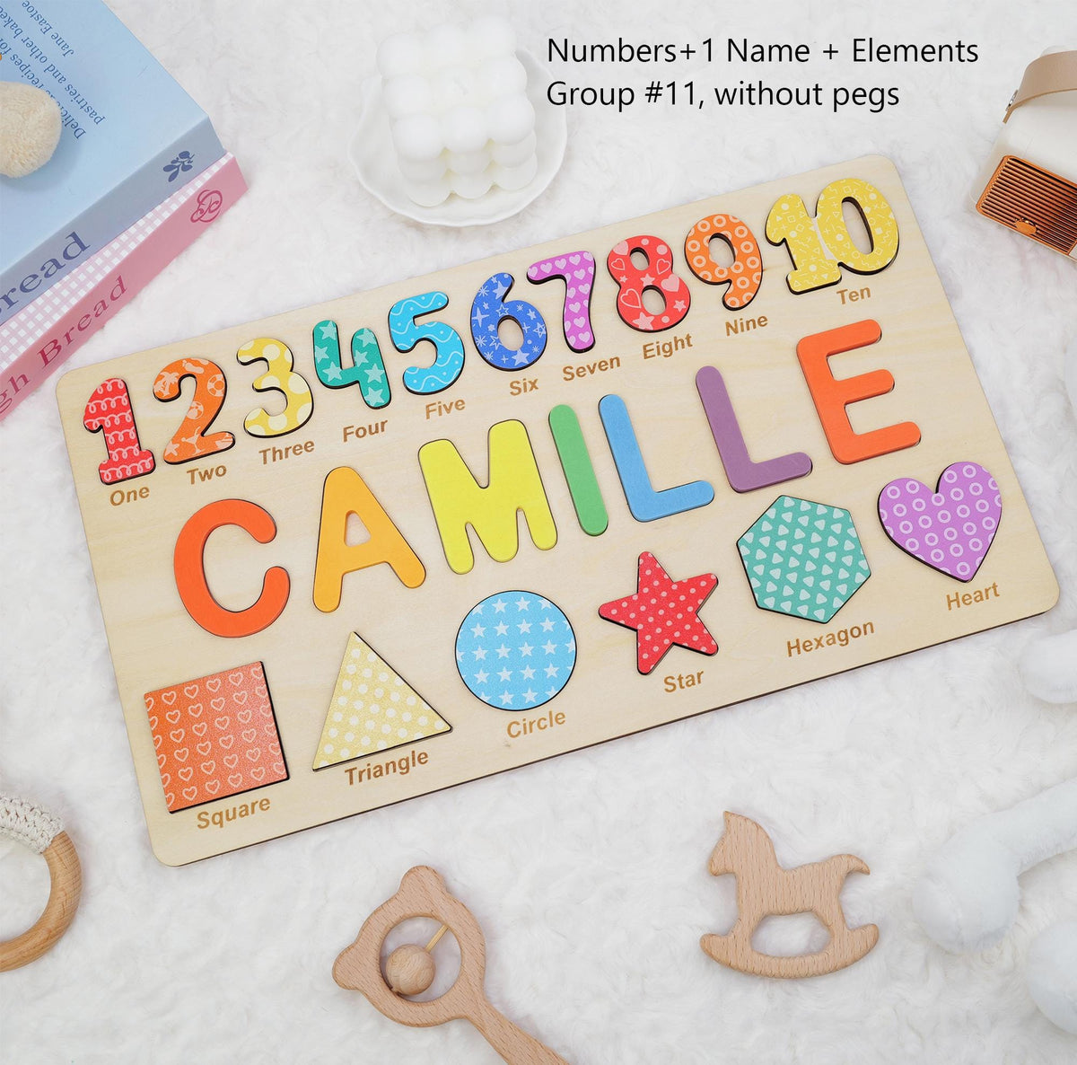 A wooden puzzle board featuring the name CAMILLE in large colorful letters, numbers one through ten, and five geometric shapes including a square, triangle, circle, star, heart, and hexagon, all with patterned surfaces and no pegs.