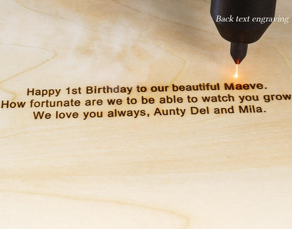 A laser engraving tool marks light-colored wood with the text: Happy 1st Birthday to our beautiful Maeve. How fortunate are we to be able to watch you grow. We love you always, Aunty Del and Mila. The text Back text engraving is visible.