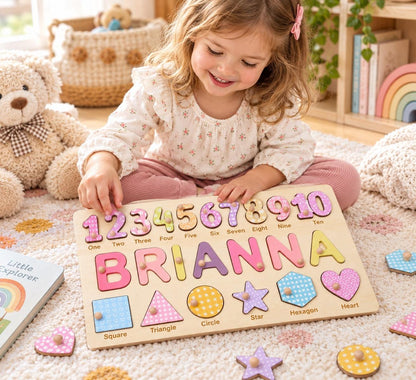 A wooden educational puzzle board featuring the name BRIANNA in large colorful letters, a row of numbers from one to ten, and a row of geometric shapes including a square, triangle, circle, star, hexagon, and heart with small knobs.