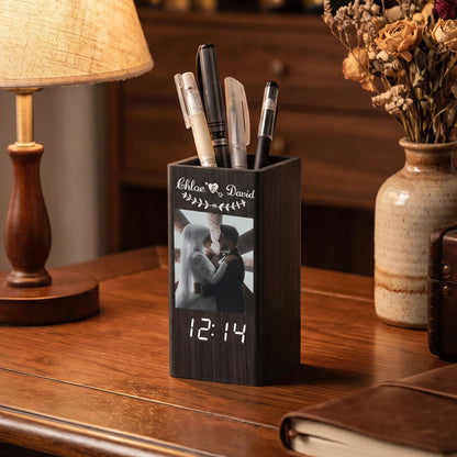 A dark wood rectangular pen holder featuring a digital clock display at the bottom and a printed photograph of a couple on the front. The text "Chloe & David" is engraved above the photo, and the holder contains four assorted pens.