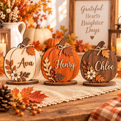 May include: Three wooden pumpkin-shaped ornaments on circular bases, each featuring a name in script font: Ava, Henry, and Chloe. Each pumpkin is decorated with layered wooden leaves, berries, and a flower, finished with a small twine bow.