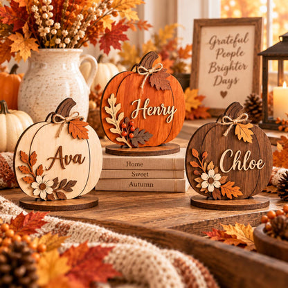 May include: Three wooden pumpkin-shaped decorations with circular bases, each featuring a name in script lettering: Ava, Henry, and Chloe. The pumpkins are finished in light, medium, and dark wood tones, adorned with small wooden leaves, flowers, and twine bows.