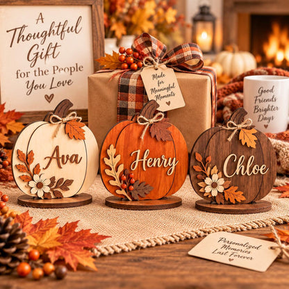 May include: Three wooden pumpkin decorations featuring the names Ava, Henry, and Chloe in script lettering. Each pumpkin is adorned with layered wooden leaves, berries, and a small twine bow. The pumpkins are displayed on circular wooden bases.