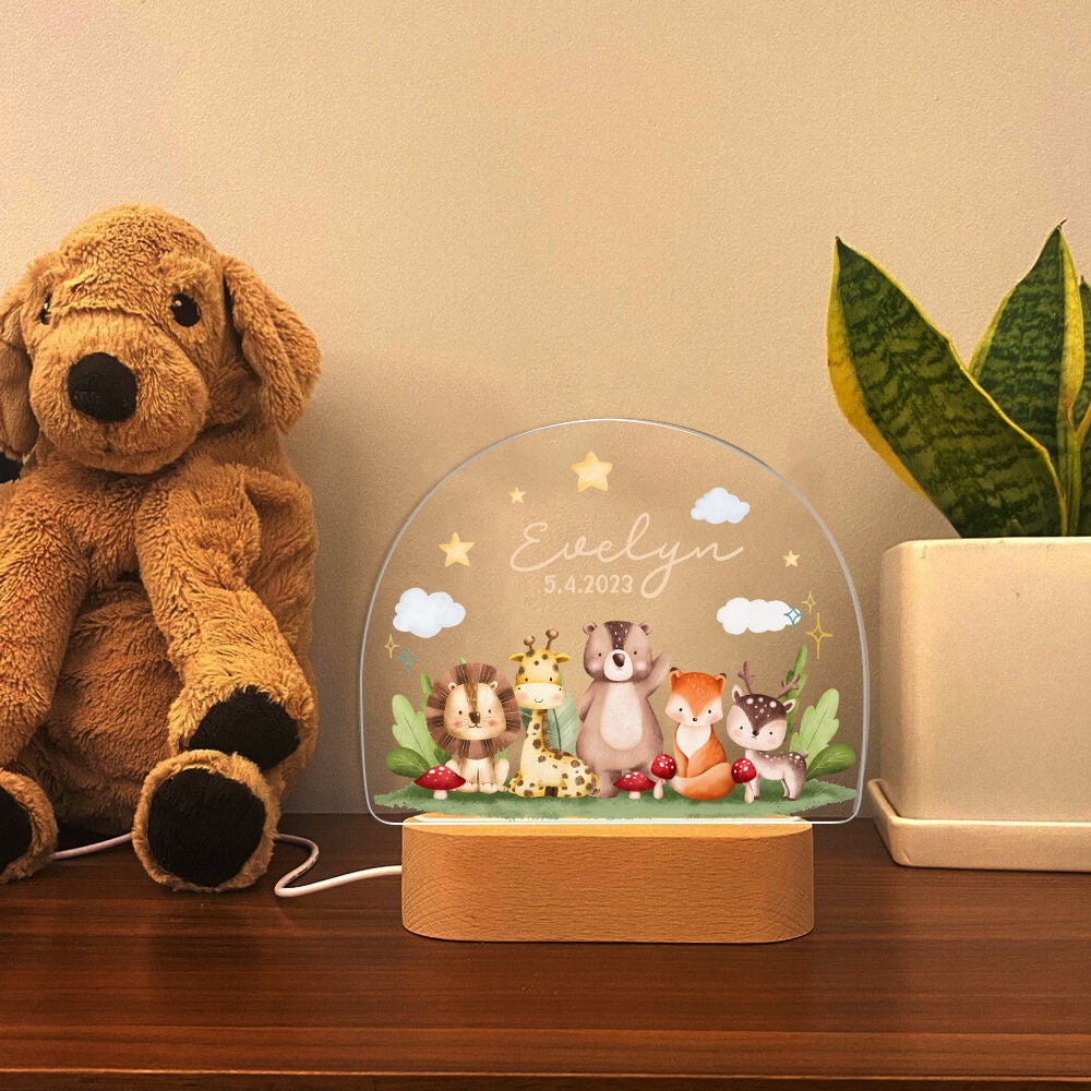 May include: A white acrylic night light with a wooden base. The light features a whimsical design of a lion, giraffe, bear, fox, and deer in a forest setting. The light is personalized with the name "Evelyn" and the date "5.4.2023".