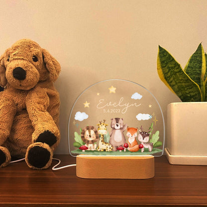 May include: A white acrylic night light with a wooden base. The light features a whimsical design of a lion, giraffe, bear, fox, and deer in a forest setting. The light is personalized with the name "Evelyn" and the date "5.4.2023".
