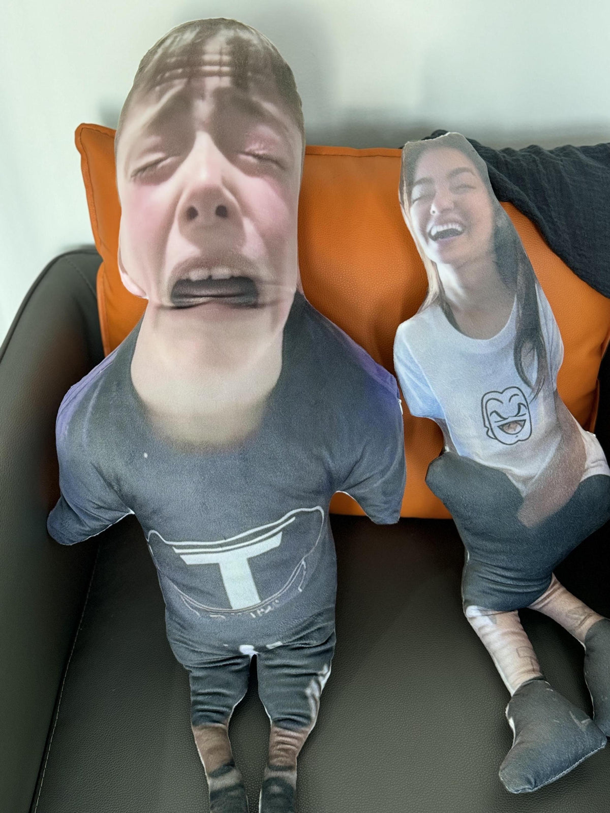 Two custom face pillows, one with a person's face making a crying expression and the other with a person's face smiling. Both pillows are wearing clothing and have limbs.