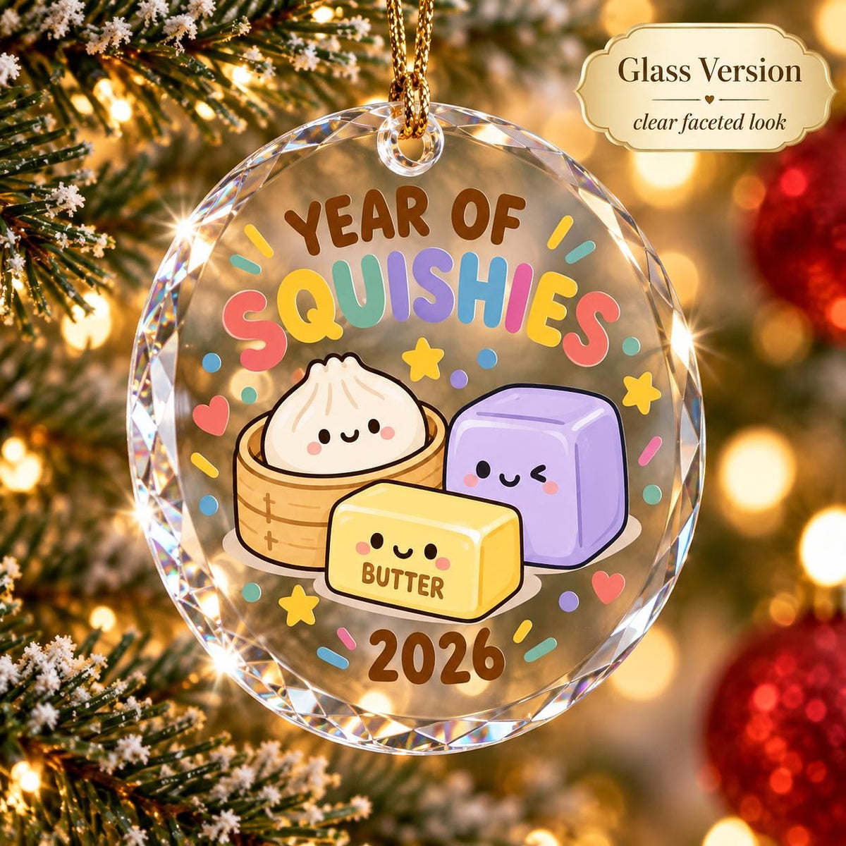 May include: A clear faceted glass circular ornament featuring the text YEAR OF SQUISHIES and 2026. The design includes a cartoon dumpling in a bamboo steamer, a purple cube, and a yellow butter block with the word BUTTER printed on it.