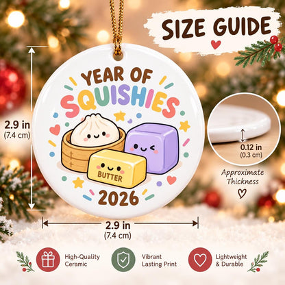 May include: A round white ceramic ornament featuring the text "YEAR OF SQUISHIES 2026" and cartoon illustrations of a dumpling, a stick of butter, and a purple cube. It measures 2.9 inches in diameter with an approximate thickness of 0.12 inches.